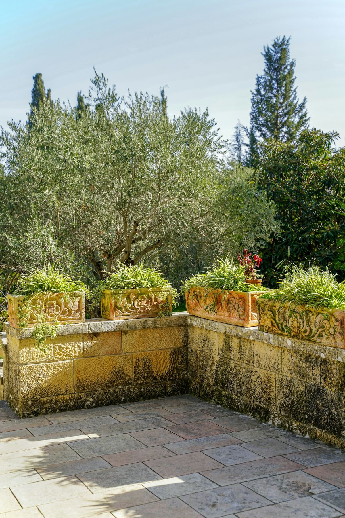 Warm sandstone-colored wall with terracotta planters above a stone-paved terrace